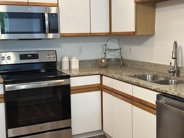 kitchen with white cabinets, a sink, stainless steel appliances, and light stone countertops