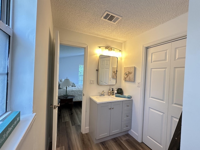 ensuite bathroom featuring a textured ceiling, visible vents, vanity, and wood finished floors