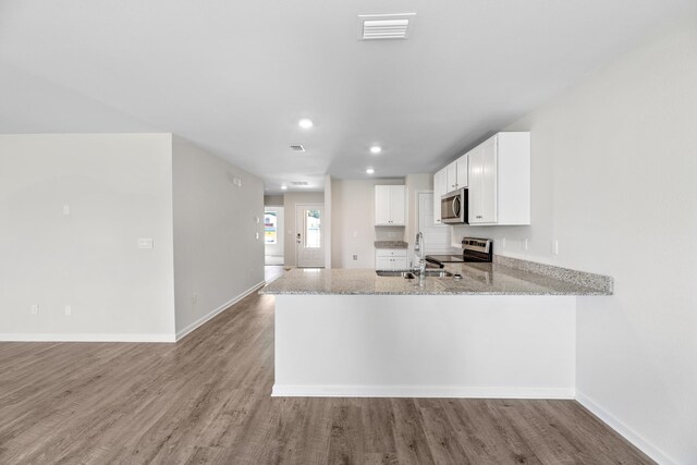 kitchen featuring kitchen peninsula, light hardwood / wood-style flooring, light stone counters, white cabinetry, and stainless steel appliances