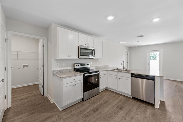 kitchen with kitchen peninsula, stainless steel appliances, sink, light hardwood / wood-style floors, and white cabinetry