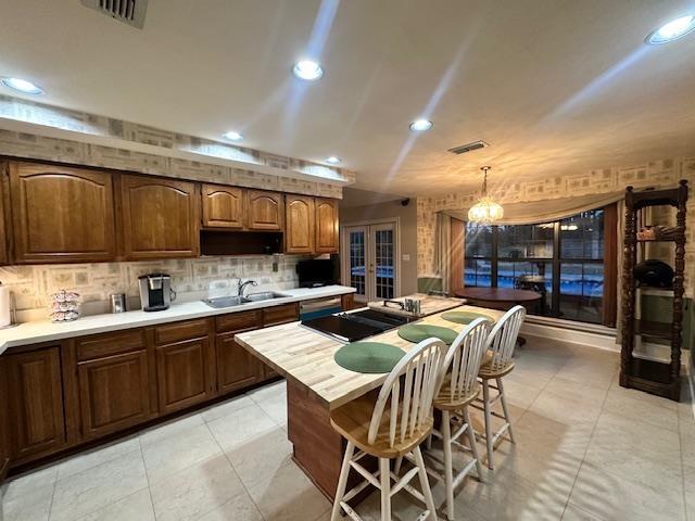 kitchen featuring sink, a breakfast bar area, black electric cooktop, decorative light fixtures, and french doors