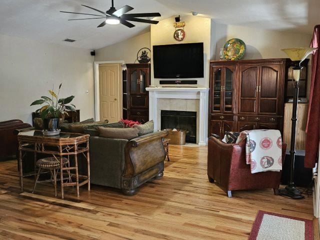 living room with light hardwood / wood-style flooring, a tile fireplace, ceiling fan, and vaulted ceiling