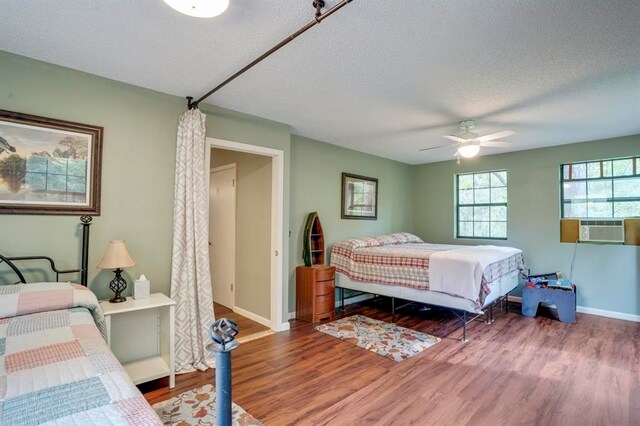 bedroom featuring cooling unit, wood-type flooring, ceiling fan, and a textured ceiling