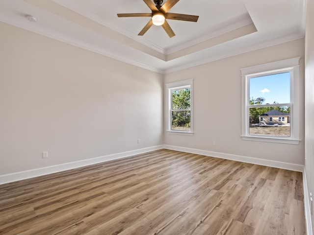 empty room with a raised ceiling, crown molding, and light hardwood / wood-style floors