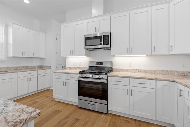 kitchen featuring white cabinetry, appliances with stainless steel finishes, light stone countertops, and light wood-type flooring