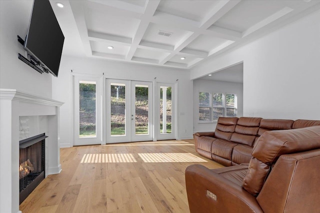 living room with beam ceiling, coffered ceiling, a fireplace, light hardwood / wood-style floors, and french doors