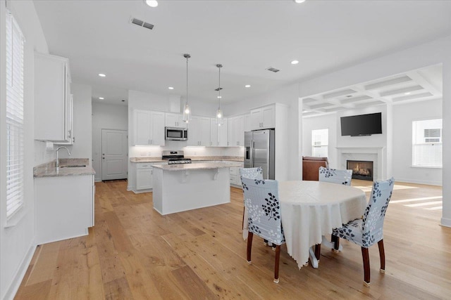 dining area featuring coffered ceiling, sink, a fireplace, and light wood-type flooring