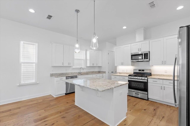 kitchen with sink, white cabinetry, decorative light fixtures, appliances with stainless steel finishes, and a kitchen island