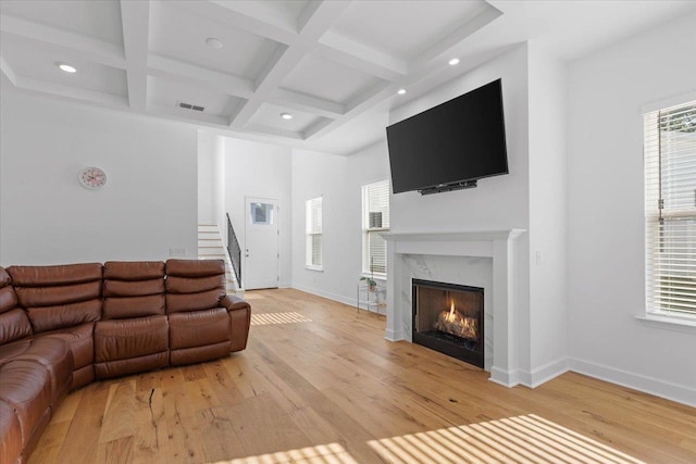 living room featuring coffered ceiling, beam ceiling, a high end fireplace, and light wood-type flooring