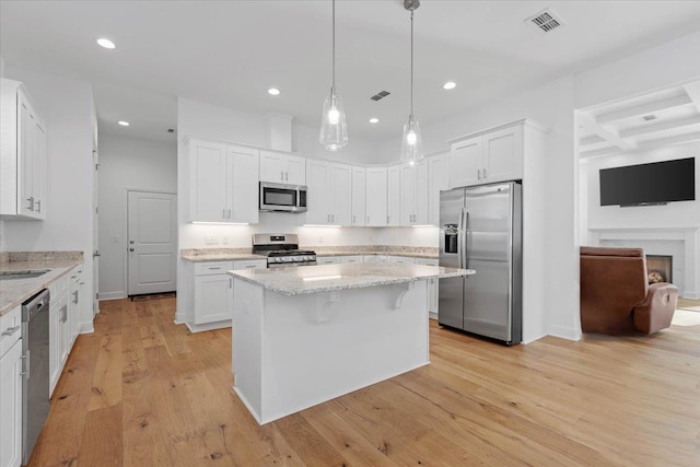 kitchen with appliances with stainless steel finishes, pendant lighting, white cabinets, and a kitchen bar