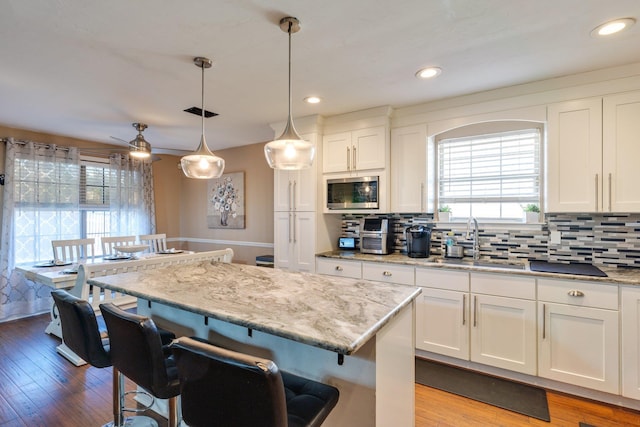 kitchen featuring a kitchen island, a sink, white cabinetry, decorative backsplash, and decorative light fixtures