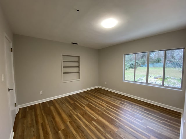 empty room featuring built in shelves and dark wood-type flooring