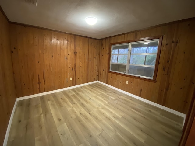 empty room featuring hardwood / wood-style flooring, crown molding, and wood walls