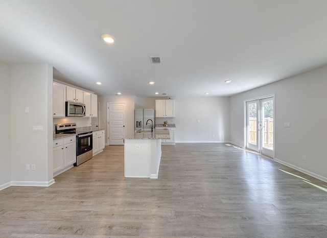 kitchen with white cabinetry, light stone counters, a center island with sink, light hardwood / wood-style flooring, and appliances with stainless steel finishes