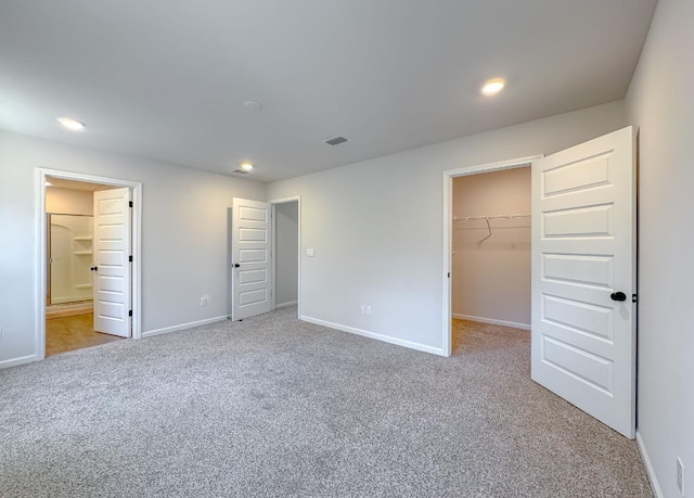 unfurnished bedroom featuring connected bathroom, a spacious closet, light carpet, and a closet