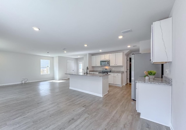 kitchen featuring white cabinetry, stainless steel appliances, light stone countertops, an island with sink, and light hardwood / wood-style floors