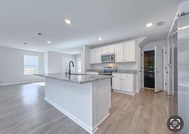 kitchen featuring sink, an island with sink, stainless steel appliances, light stone countertops, and white cabinets