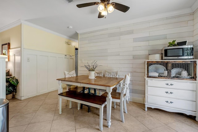 tiled dining room with ceiling fan, wood walls, and crown molding