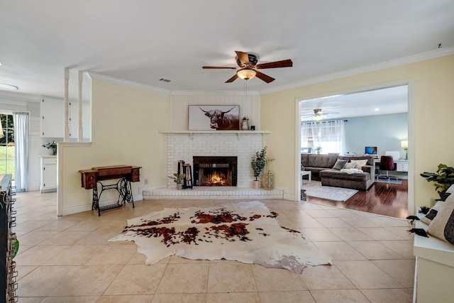 living room with ceiling fan, light tile patterned floors, ornamental molding, and a brick fireplace