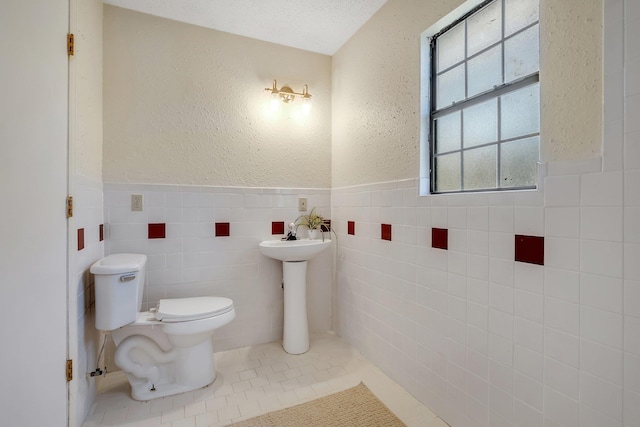 bathroom with tile patterned floors, sink, toilet, tile walls, and a textured ceiling