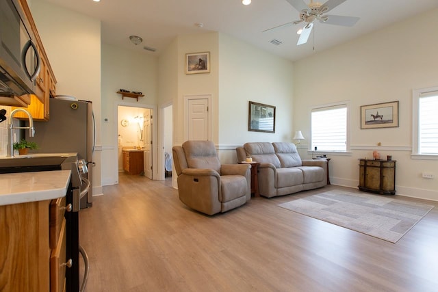 living room with ceiling fan, light hardwood / wood-style flooring, and high vaulted ceiling