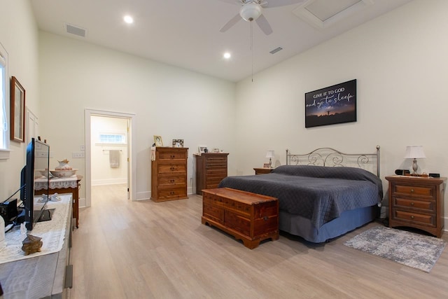 bedroom featuring connected bathroom, ceiling fan, light hardwood / wood-style flooring, multiple windows, and a high ceiling