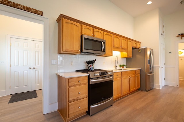 kitchen featuring tasteful backsplash, appliances with stainless steel finishes, sink, and light hardwood / wood-style flooring