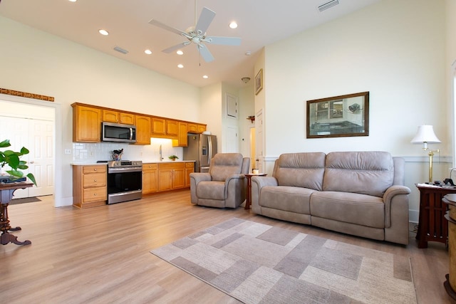 living room featuring a high ceiling, ceiling fan, and light hardwood / wood-style floors