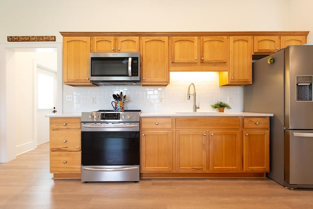 kitchen with sink, appliances with stainless steel finishes, decorative backsplash, and light hardwood / wood-style flooring