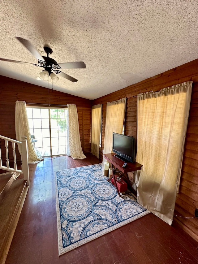 unfurnished room with a textured ceiling, dark hardwood / wood-style floors, wooden walls, vaulted ceiling, and ceiling fan