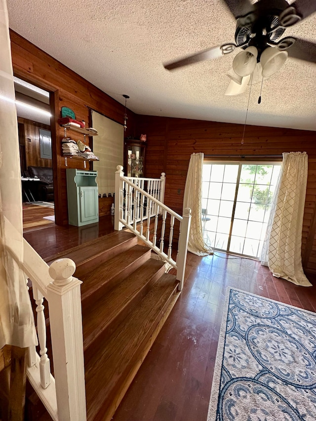 staircase with wood walls, wood-type flooring, a textured ceiling, and ceiling fan