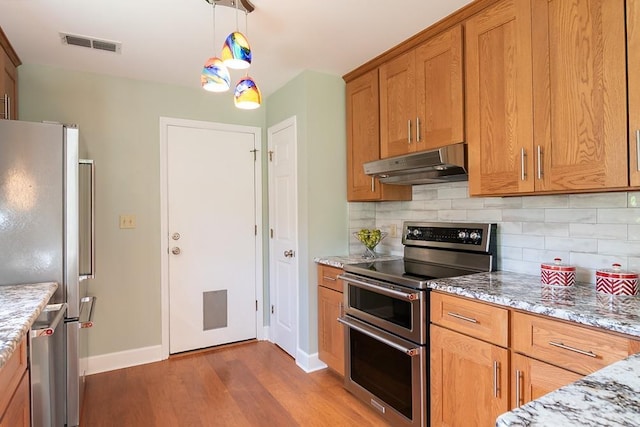 696 Lupine Ln, Tallahassee, FL 32308 - kitchen featuring stainless steel appliances, under cabinet range hood, dark wood-style flooring, decorative backsplash, and brown cabinets