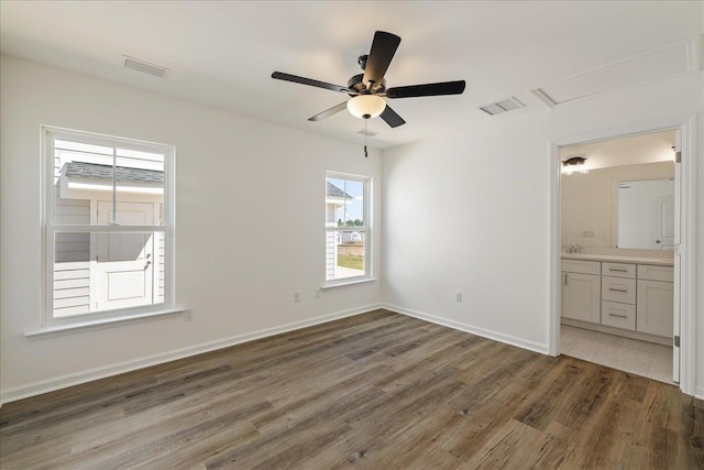 unfurnished bedroom with multiple windows, dark wood-type flooring, connected bathroom, and ceiling fan