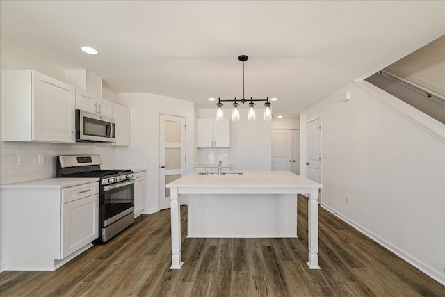 kitchen with a breakfast bar, appliances with stainless steel finishes, white cabinetry, a center island with sink, and decorative light fixtures