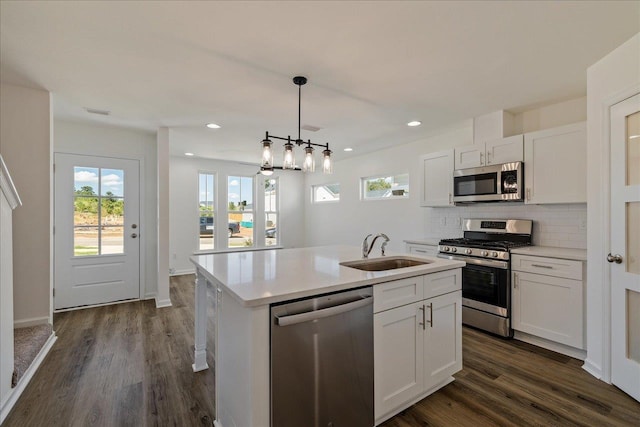 kitchen with appliances with stainless steel finishes, pendant lighting, white cabinetry, sink, and a kitchen island with sink