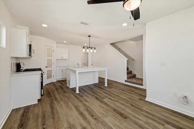 kitchen with white cabinetry, hanging light fixtures, a center island with sink, stainless steel appliances, and backsplash