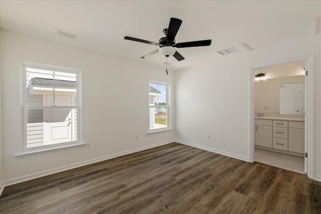 unfurnished bedroom with multiple windows, dark wood-type flooring, connected bathroom, and ceiling fan