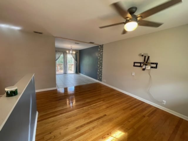 empty room with ceiling fan with notable chandelier and light hardwood / wood-style flooring