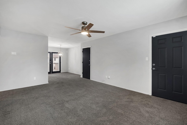 empty room featuring dark colored carpet and ceiling fan with notable chandelier