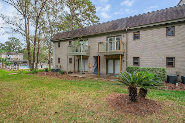 back of property with a lawn, central AC unit, and a balcony