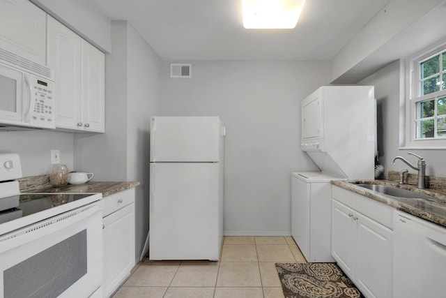 kitchen featuring white appliances, stacked washer and clothes dryer, sink, light tile patterned floors, and white cabinetry