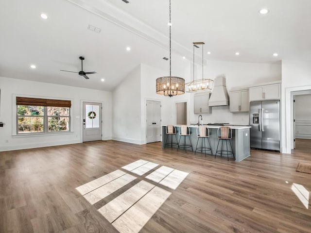 kitchen with decorative light fixtures, stainless steel appliances, beamed ceiling, a kitchen island with sink, and custom range hood