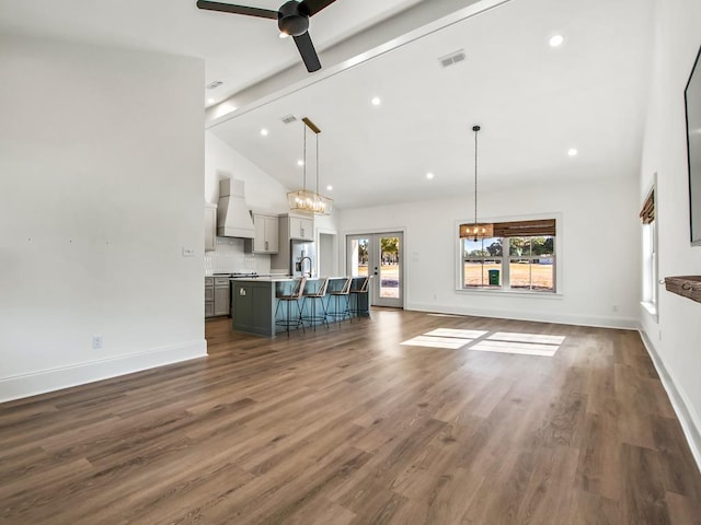 unfurnished living room featuring french doors, ceiling fan with notable chandelier, vaulted ceiling with beams, and dark hardwood / wood-style flooring