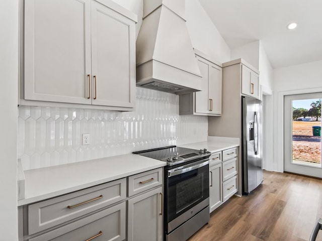 kitchen with custom exhaust hood, stainless steel appliances, backsplash, dark hardwood / wood-style floors, and gray cabinetry