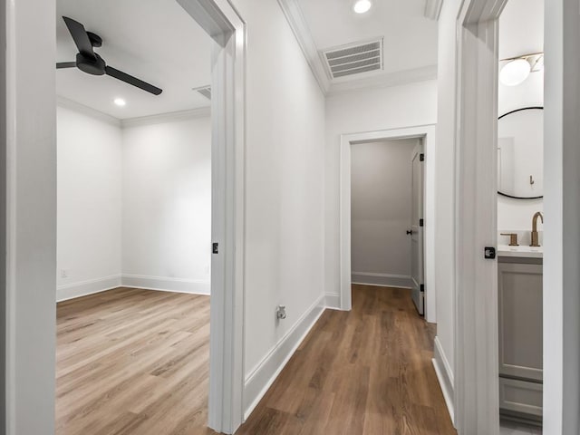 hallway featuring sink, ornamental molding, and light wood-type flooring