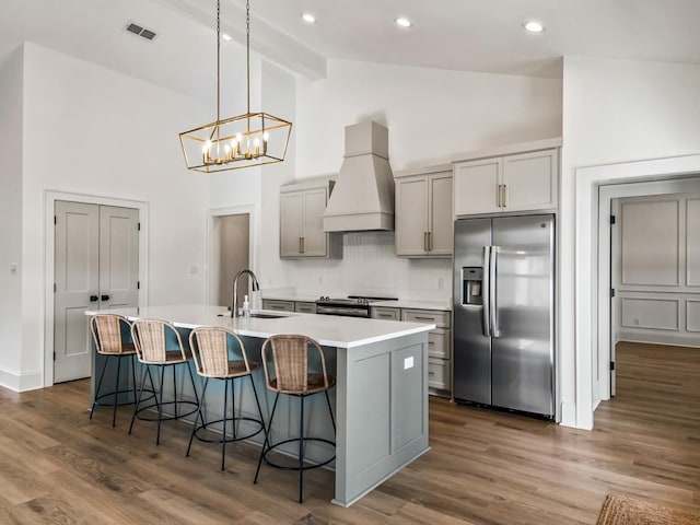 kitchen with stainless steel appliances, premium range hood, backsplash, gray cabinets, and a kitchen island with sink