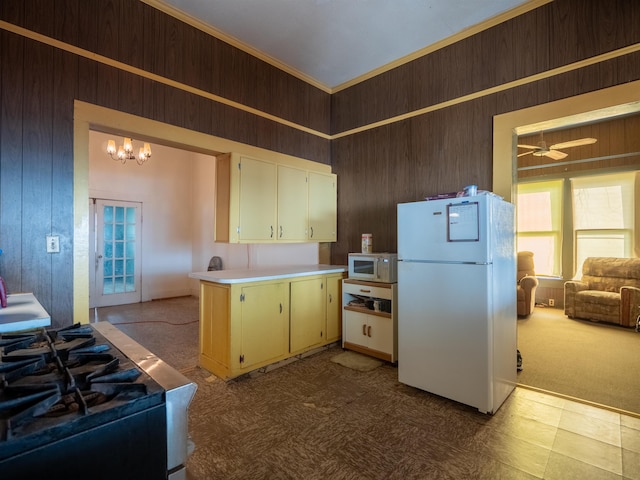 kitchen with ceiling fan with notable chandelier, white appliances, light colored carpet, and wood walls