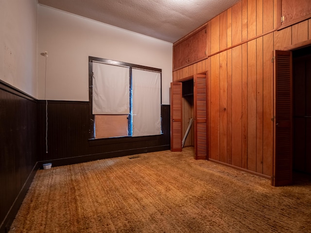 carpeted empty room featuring a textured ceiling and wooden walls