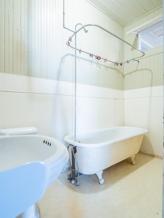 bathroom featuring wood walls, toilet, a tub, and concrete floors