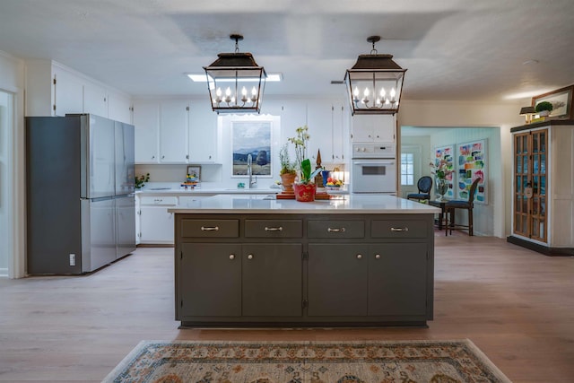 kitchen with stainless steel refrigerator, white cabinetry, a kitchen island, decorative light fixtures, and oven